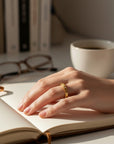 Anillo argolla de plata enchapada en oro de Sophia Schneider Joyas con textura y circones, en mano sobre cuaderno abierto.