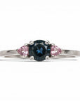 Anillo Sophia Schneider Joyas de platino con diamante negro central y zafiros rosados triangulares a cada lado.