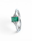 Anillo Sophia Schneider Joyas de platino con esmeralda rectangular central y diamantes laterales.