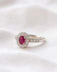 Anillo solitario de platino con rubí ovalado central y halo de diamantes, de Sophia Schneider Joyas.