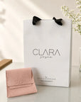 Bolsa de regalo blanca y estuche de gamuza rosa de Sophia Schneider Joyas sobre una mesa con flores