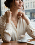 Collar Sophia Schneider Joyas con círculo de diamantes y cadena de oro 18K lucido por una mujer en una cafetería