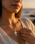 Colgante de cruz en lámina de oro 18K de Sophia Schneider Joyas lucido por una mujer en la playa al atardecer