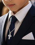 Niño con traje azul y corbata usando una cruz de plata 925 de Sophia Schneider Joyas en una ceremonia religiosa