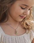 Niña luciendo medalla redonda de Sophia Schneider Joyas con Virgen orando en plata y oro laminado de 12 mm