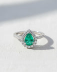 Anillo de platino Sophia Schneider Joyas con esmeralda central corte gota y halo de brillantes en la argolla.