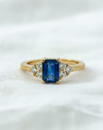 Anillo Sophia Schneider Joyas de oro amarillo 18K con zafiro central octogonal azul y diamantes corte brillante a cada lado.