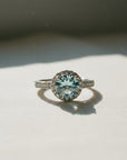 Sophia Schneider Joyas sterling silver ring with 2 ct round blue topaz center stone surrounded by small clear stones.