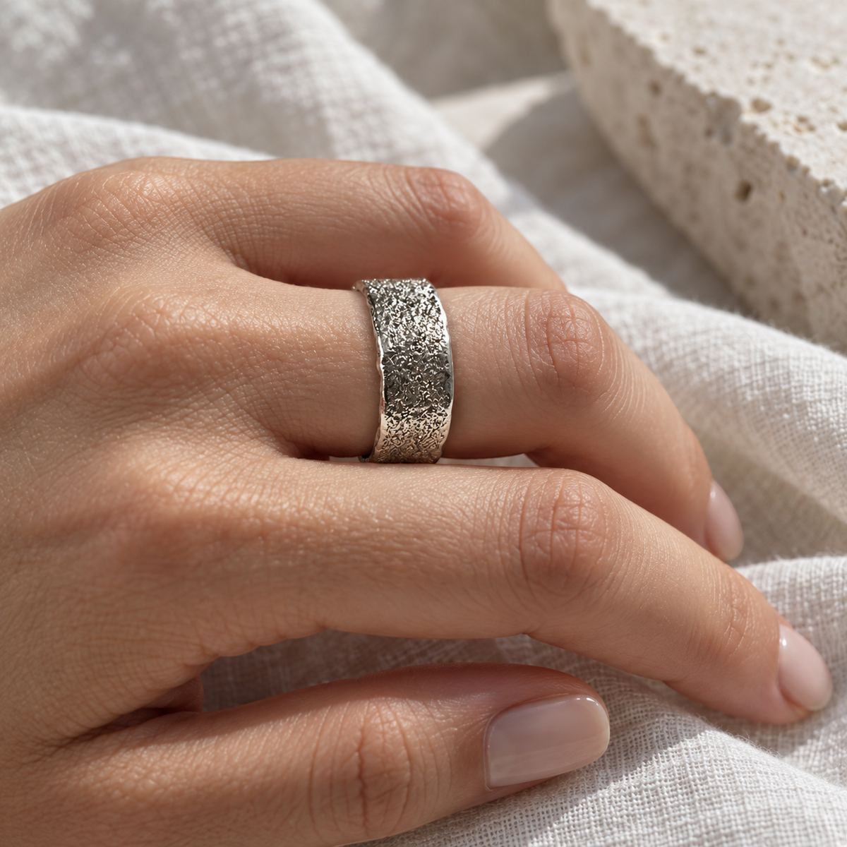 Anillo banda ajustable de 7 mm en plata con textura rugosa y bordes lisos de Sophia Schneider Joyas en una mano