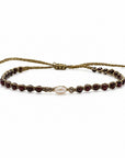 Pulsera ajustable ClaraJoyas de hilo dorado con perla central y cuentas de granate rojo sobre fondo blanco