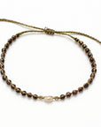 Pulsera ajustable ClaraJoyas con hilo dorado, cuentas de granate rojo y una perla central blanca