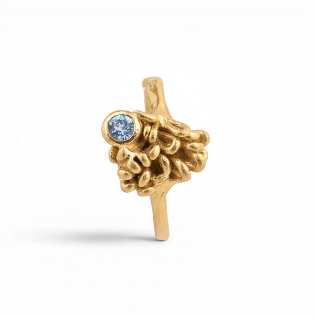 Sophia Schneider Joyas 18K gold ring with a small blue tanzanite gemstone and organic, textured detailing.