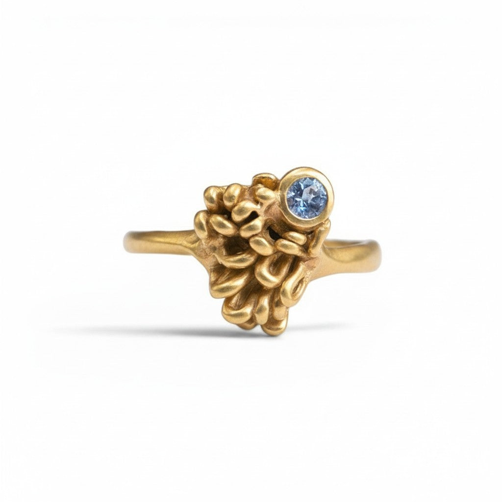 Sophia Schneider Joyas 18K gold ring with a textured, organic design and a small round blue tanzanite gemstone.