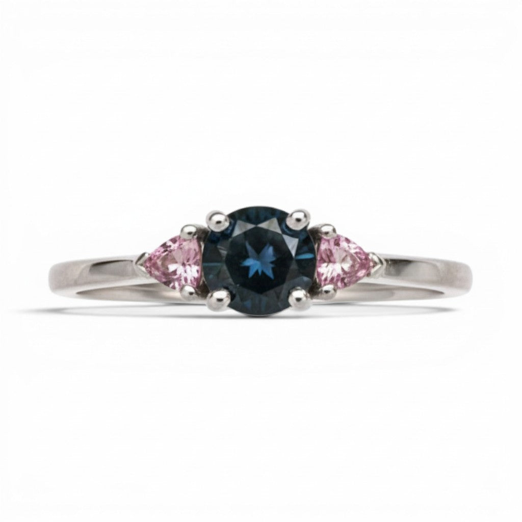 Anillo Sophia Schneider Joyas de platino con diamante negro central y zafiros rosados triangulares a cada lado.