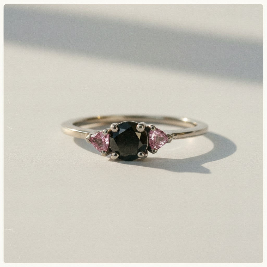Anillo Sophia Schneider Joyas de platino con diamante negro central y zafiros rosados laterales.