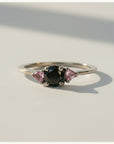 Anillo Sophia Schneider Joyas de platino con diamante negro central y zafiros rosados laterales.