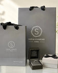 Anillo solitario con diamante ovalado de Sophia Schneider Joyas en estuche junto a bolsas de regalo grises