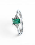 Anillo Sophia Schneider Joyas de platino con esmeralda rectangular central y diamantes laterales.