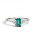 Anillo solitario de platino Sophia Schneider Joyas con esmeralda rectangular verde y diamantes laterales.