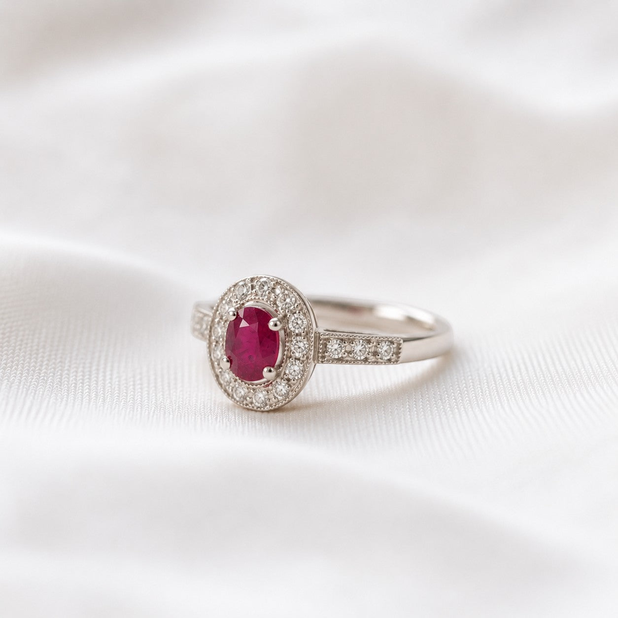 Anillo solitario de platino con rubí ovalado central y halo de diamantes, de Sophia Schneider Joyas.