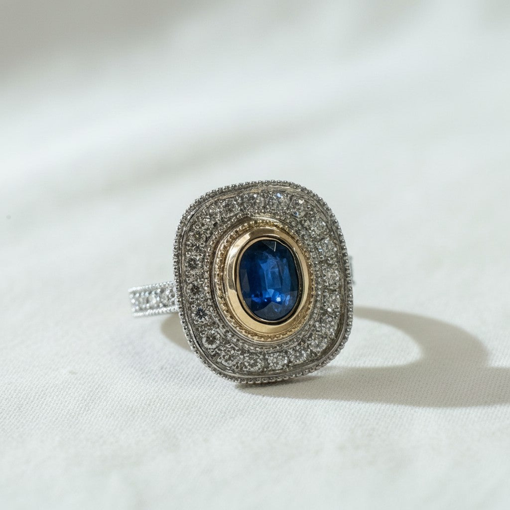 Anillo Sophia Schneider Joyas de platino y oro amarillo 18K con zafiro oval azul central y halo de diamantes brillantes.
