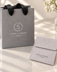 Bolsa de regalo y estuche de Sophia Schneider Joyas en color gris con logo impreso sobre una mesa blanca
