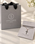 Colgante de cruz en plata 925 de Sophia Schneider Joyas presentado en una bolsa y estuche de regalo gris elegante