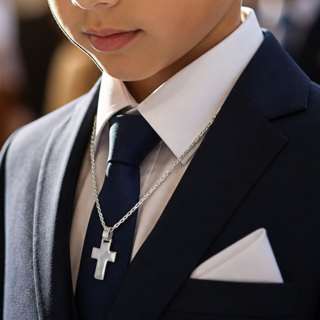 Niño con traje azul y corbata usando una cruz de plata 925 de Sophia Schneider Joyas en una ceremonia religiosa