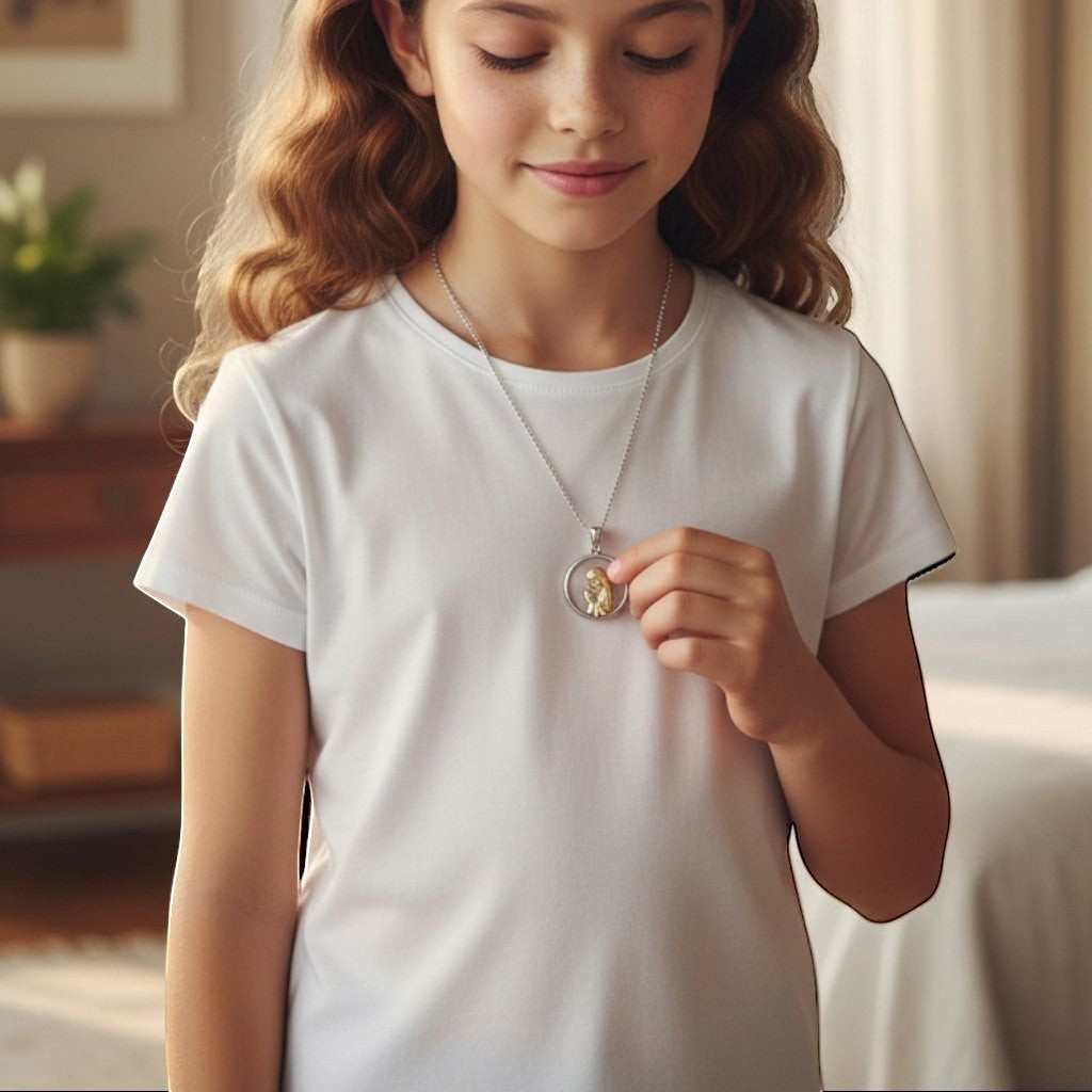 Niña luciendo medalla redonda de la Virgen orando en plata y oro laminado de Sophia Schneider Joyas
