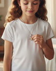 Niña luciendo medalla redonda de la Virgen orando en plata y oro laminado de Sophia Schneider Joyas