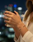 Pulsera esclava lisa de plata de Sophia Schneider Joyas en la muñeca de una mujer con fondo urbano nocturno