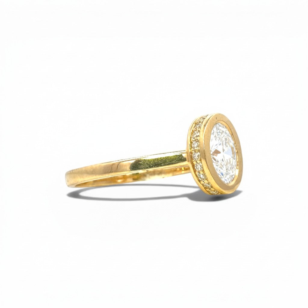Sophia Schneider Joyas 18K gold ring with 1 ct oval lab-grown diamond, bezel set with pavé diamonds.