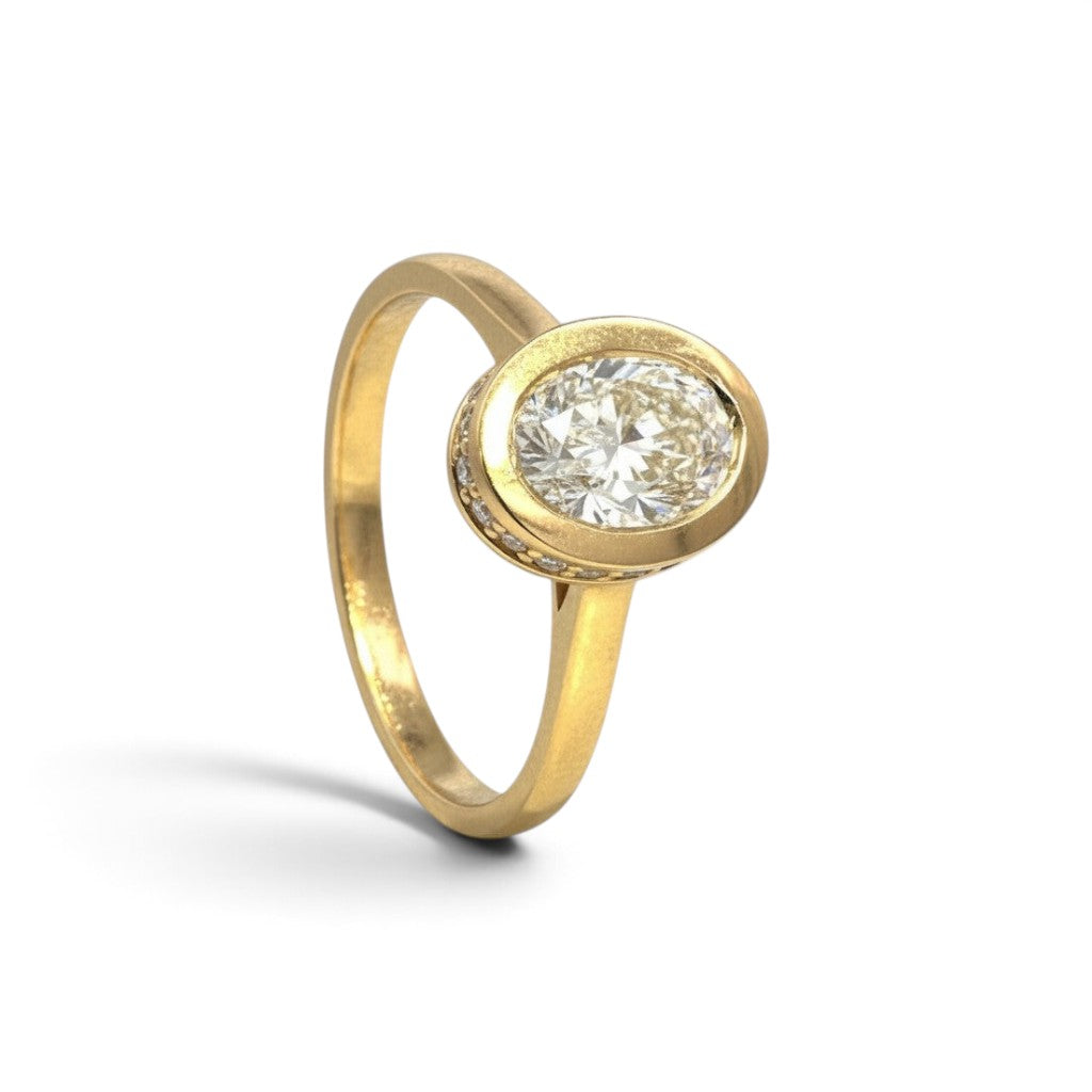 Sophia Schneider Joyas 18K yellow gold ring with 1 ct oval lab-grown diamond, bezel set with small accent diamonds.
