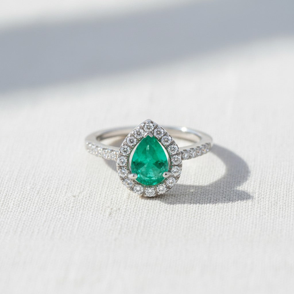 Anillo de platino Sophia Schneider Joyas con esmeralda central corte gota y halo de brillantes en la argolla.