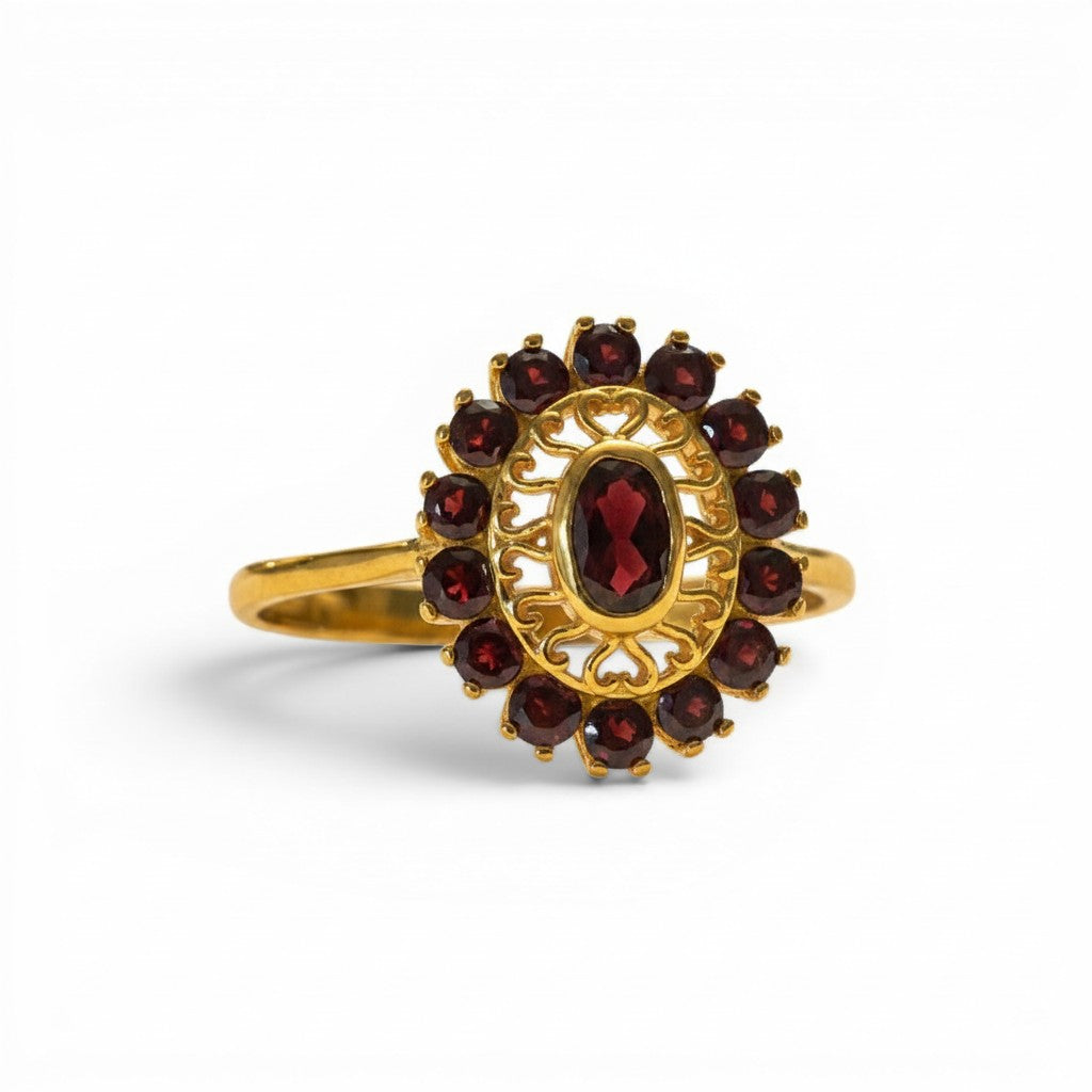 Sophia Schneider Joyas 14K gold ring with oval garnet center stone surrounded by a halo of smaller garnets in a floral design.
