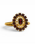Sophia Schneider Joyas 14K gold ring with oval garnet center stone surrounded by a halo of smaller garnets in a floral design.