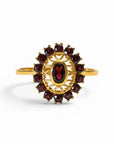 Sophia Schneider Joyas 14K gold ring with oval garnet center stone surrounded by a halo of smaller garnets in a floral design.